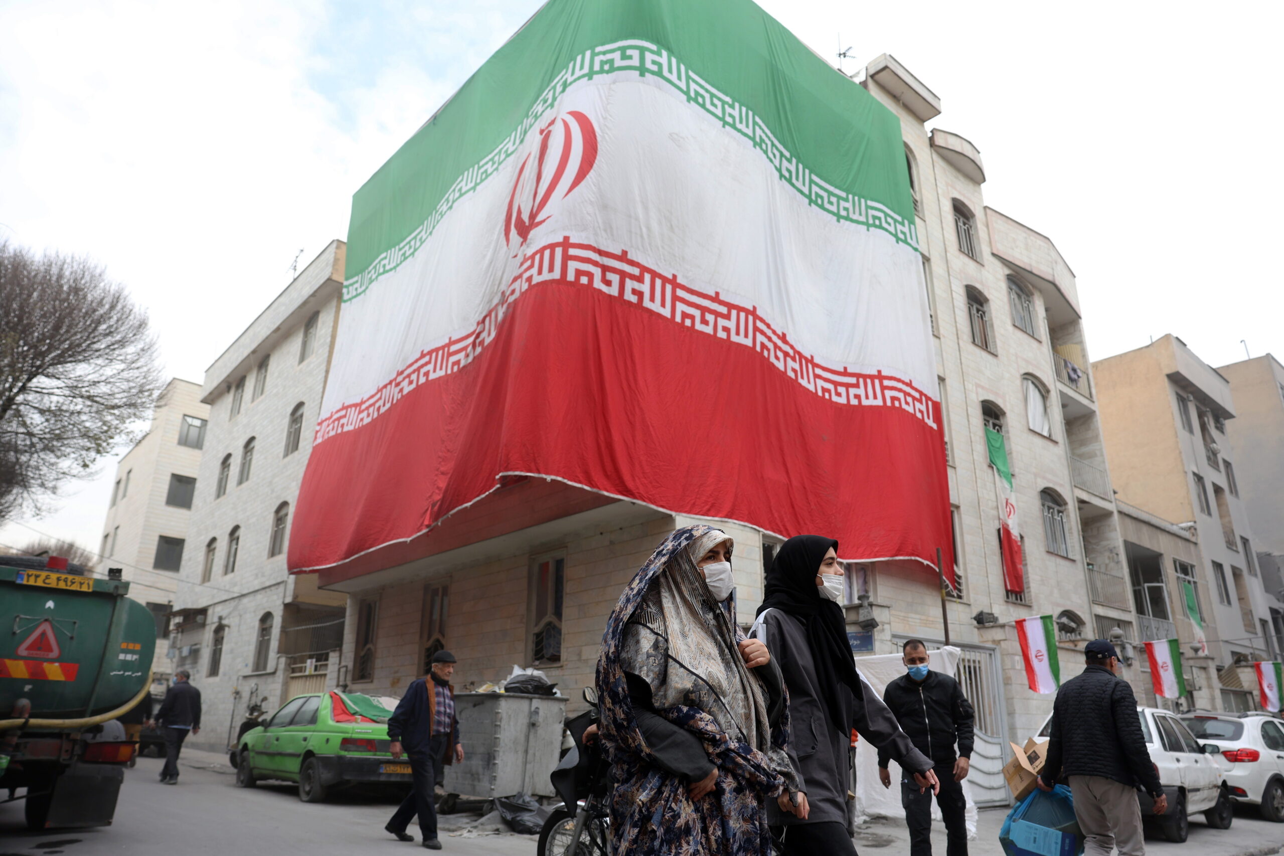 Iranians walk next to damaged residential buildings covered by Iran's national flag in southern Tehran, Iran, 15 March 2026. A joint Israeli and US military operation continues to target multiple locations across Iran since the early hours of 28 February 2026.