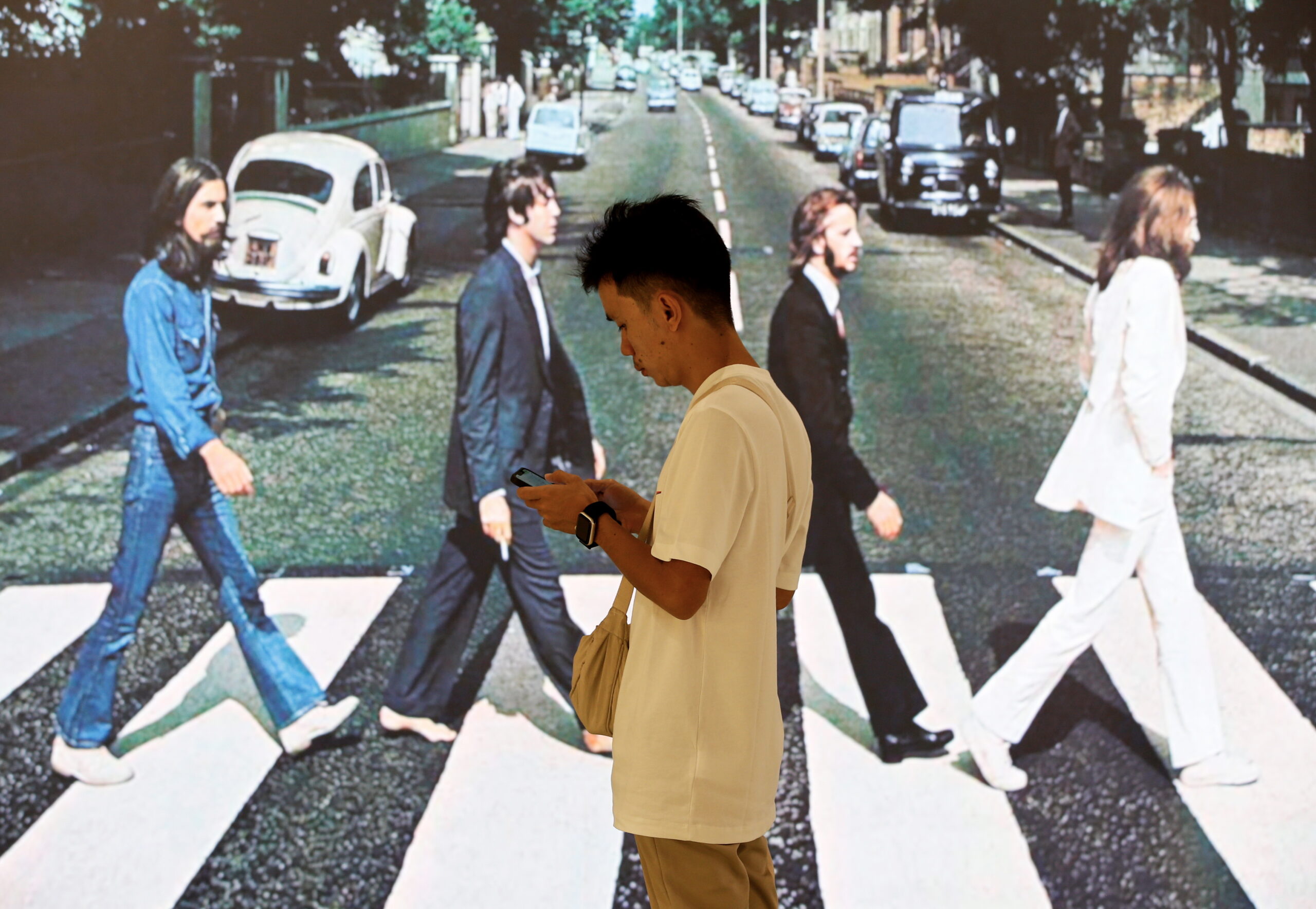 A fan of the Beatles uses a mobile phone next to a screen displaying the cover of The Beatles album 'Abbey Road' during an event to promote the band's newly released and last song 'Now And Then' in Bangkok, Thailand, 23 November 2023. The record label Universal Music Thailand held an event to promote the new and ‘the last Beatles song’, Now And Then, which has been created with the aid of artificial intelligence to separate John Lennon’s vocals from a demo tape he recorded in the late 1970s, and features guitar parts recorded by George Harrison in 1995.
