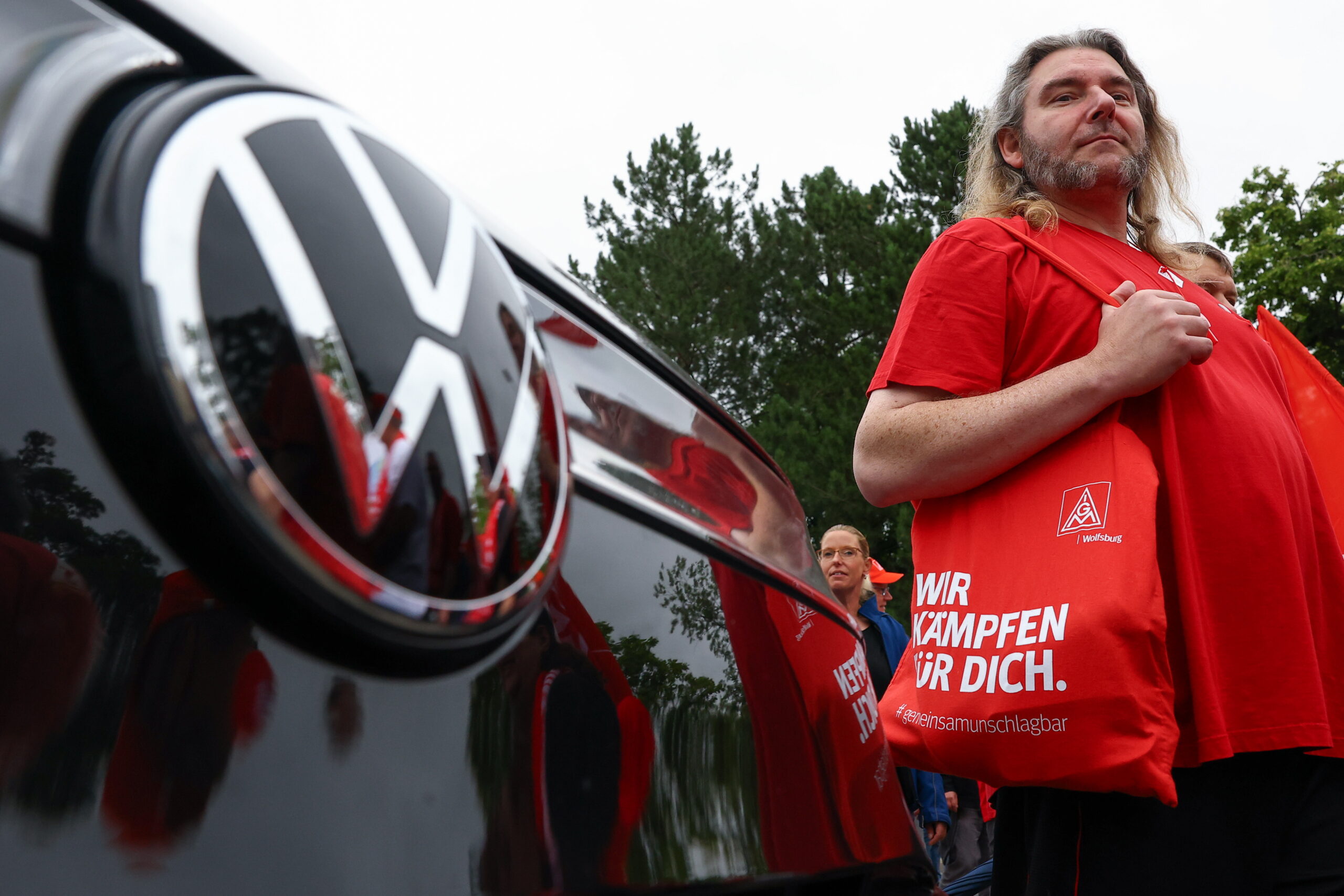 People stand next to a Volkswagen vehicle as the carmaker's employees and IG Metall union members rally on the grounds of the Volkswagen headquarters on the day of a supervisory board meeting, in Wolfsburg, Germany, 09 July 2026.