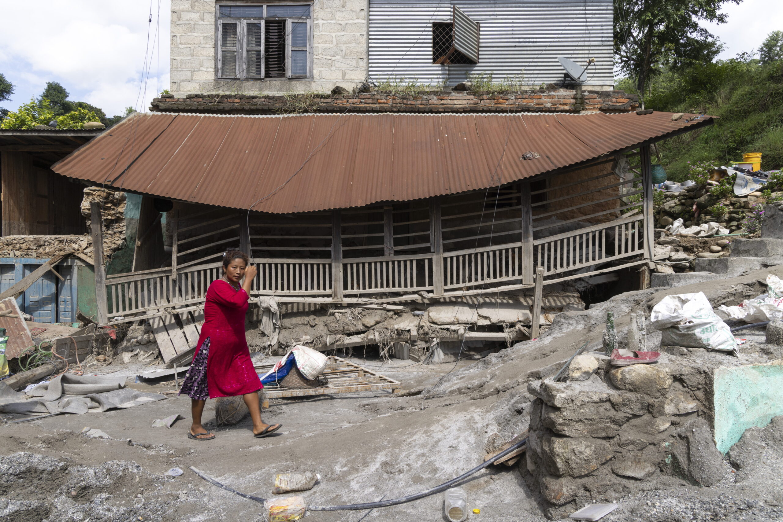 epa13200028 A woman walks in front of a damaged house following flash floods along the banks of the Trishuli River in Dhading district, Nepal, 30 August 2026. More than 700 people were killed, and hundreds remain missing across northern Nepal after a glacial collapse and avalanche triggered flash floods and mudslides along the Bhotekoshi and Trishuli river valleys near the Nepal-Tibet border, causing widespread destruction to settlements and infrastructure, according to the National Disaster Risk Reduction and Management Authority (NDRRMA).
