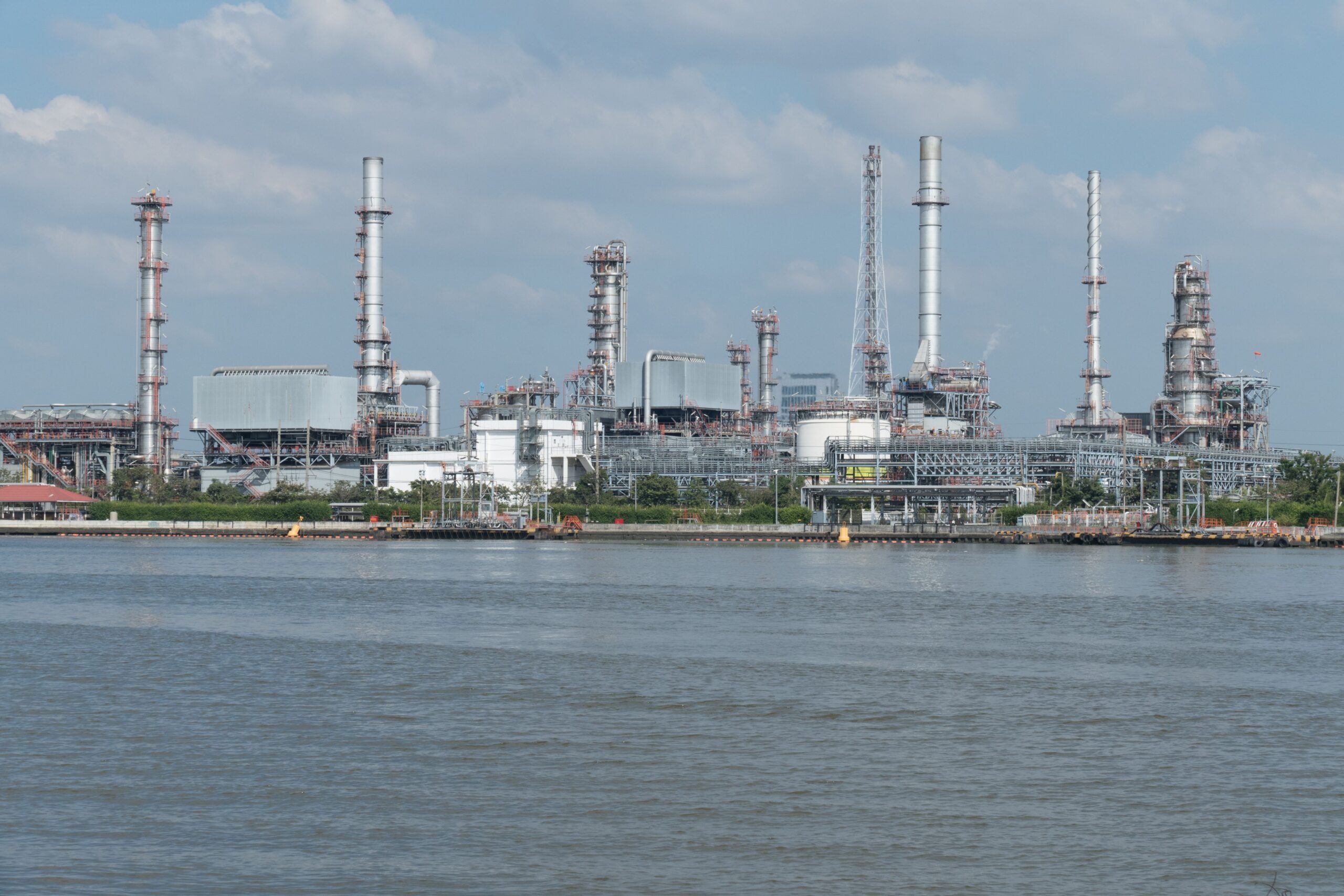 A large oil refinery complex next to the water with cloudy skies.