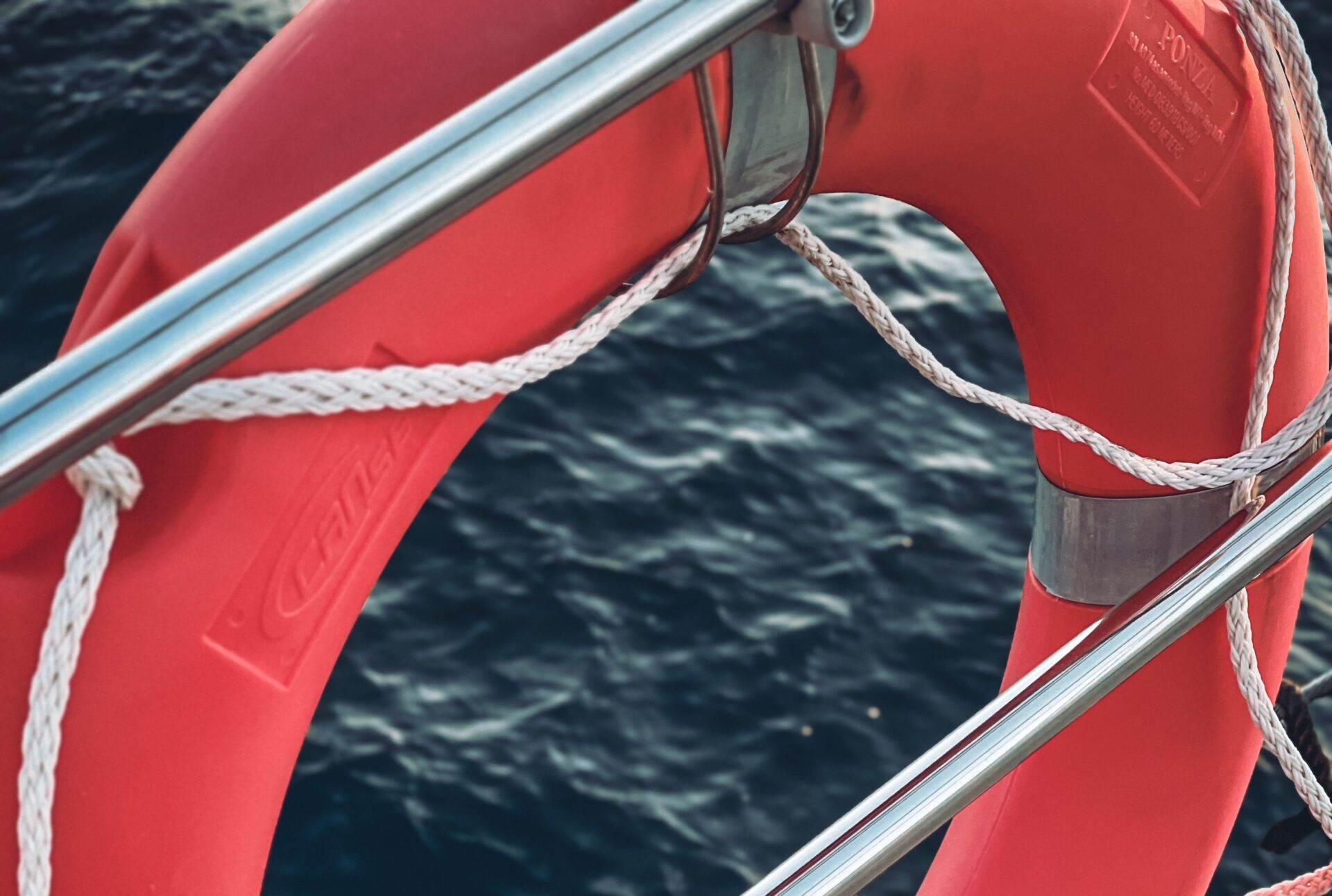 A vibrant pink lifebuoy attached to a yacht railing over the deep blue sea in Athens, Greece.