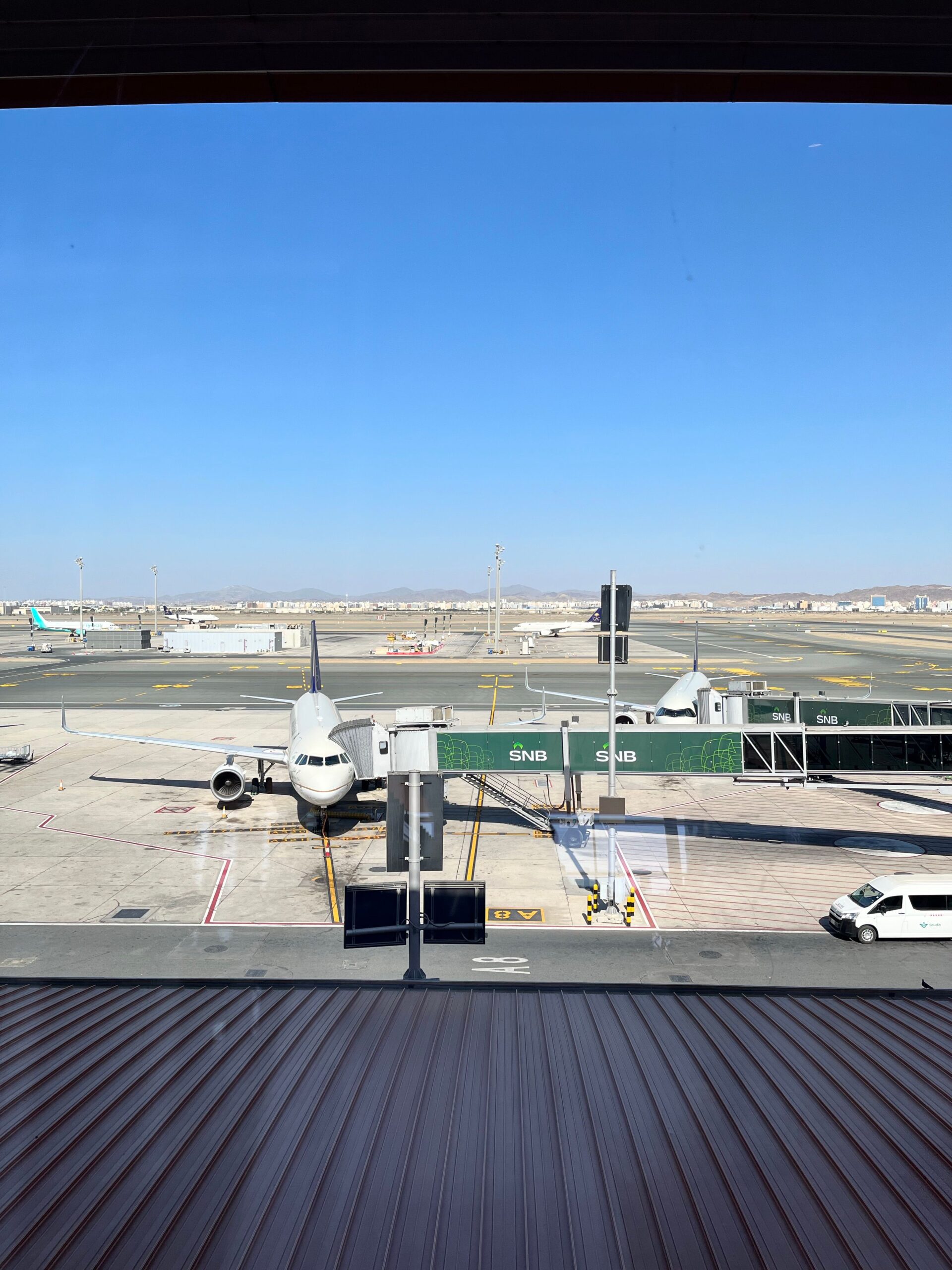 Airplane docked at terminal gate in Jeddah Airport, clear blue sky.